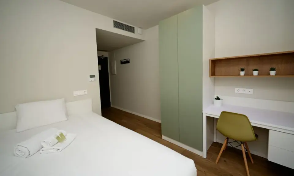 Habitación moderna con cama, armario verde y escritorio. Un espacio acogedor en Xior The Lofttown, listo para tu estancia.