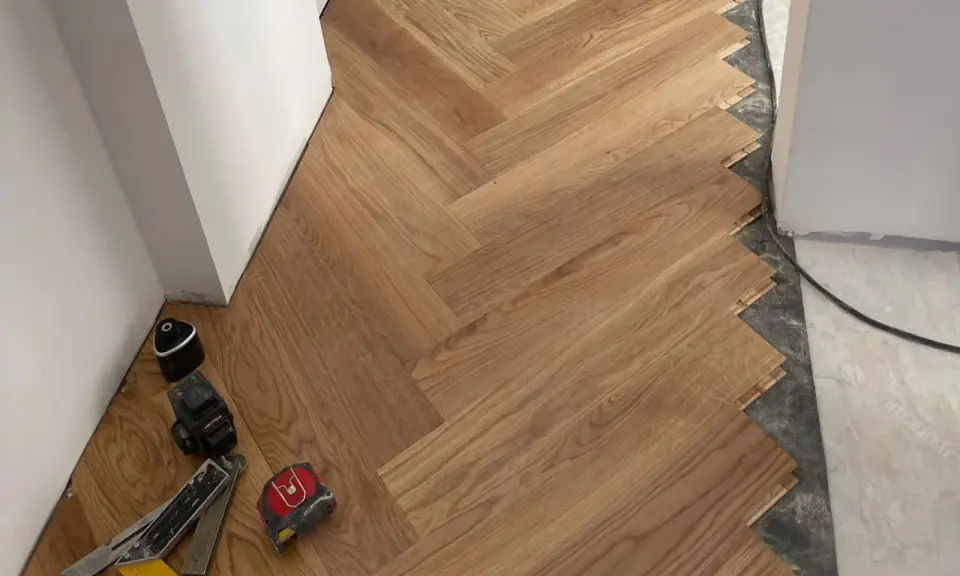 Instalación de suelo de madera en espiga. El rodapié igual que el suelo crea un acabado moderno y continuo. Herramientas de instalación a la vista.