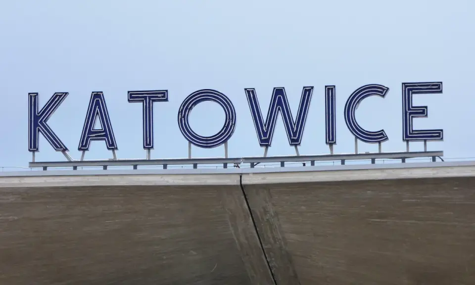 Napis "KATOWICE" z niebieskimi neonami na tle nieba, nad betonową konstrukcją.
