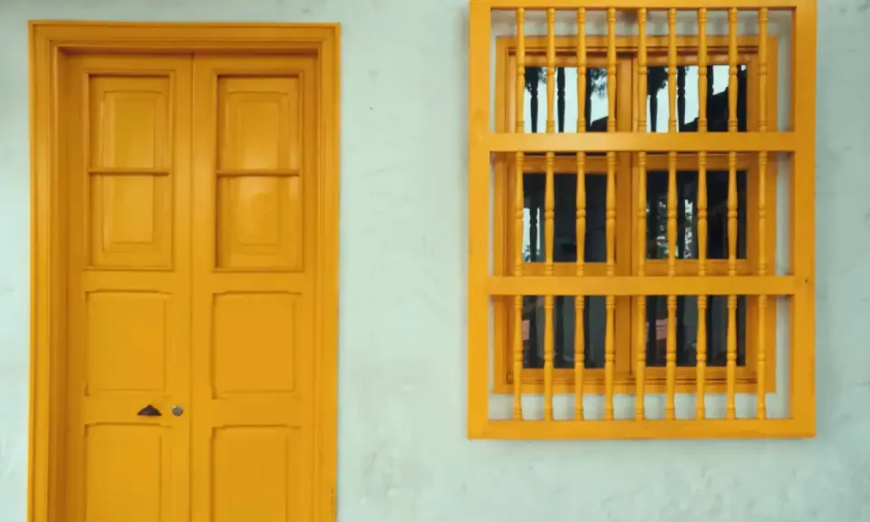 Une porte et une fenêtre avec un encadrement de porte couleur différente, le tout peint en jaune vif sur un mur blanc texturé.