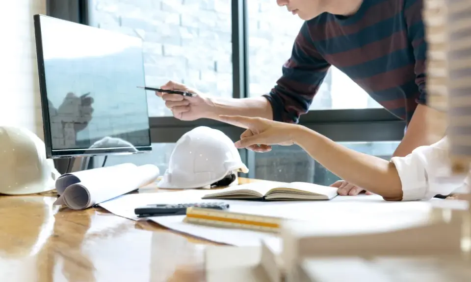Deux architectes discutent d'un plan sur un écran, utilisant un système de gestion de contenu d'entreprise pour organiser leurs documents.