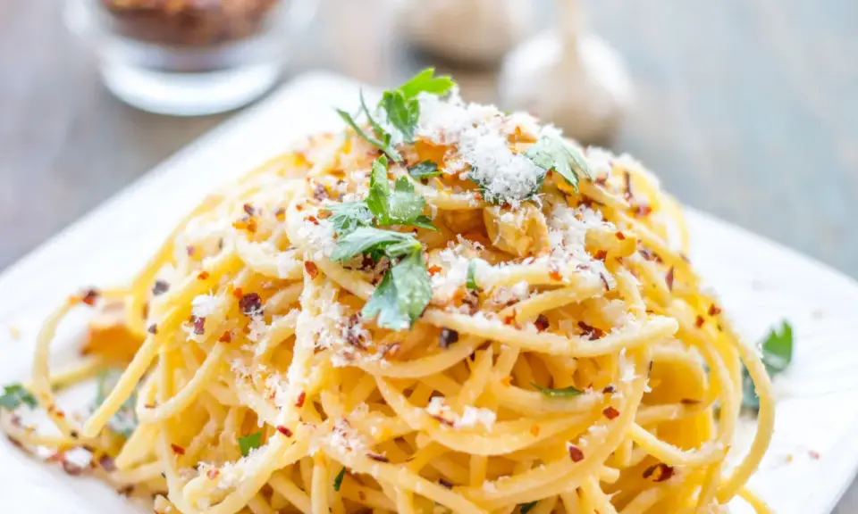Pyszne spaghetti aglio olio, posypane parmezanem i natką pietruszki, z płatkami chili w tle.
