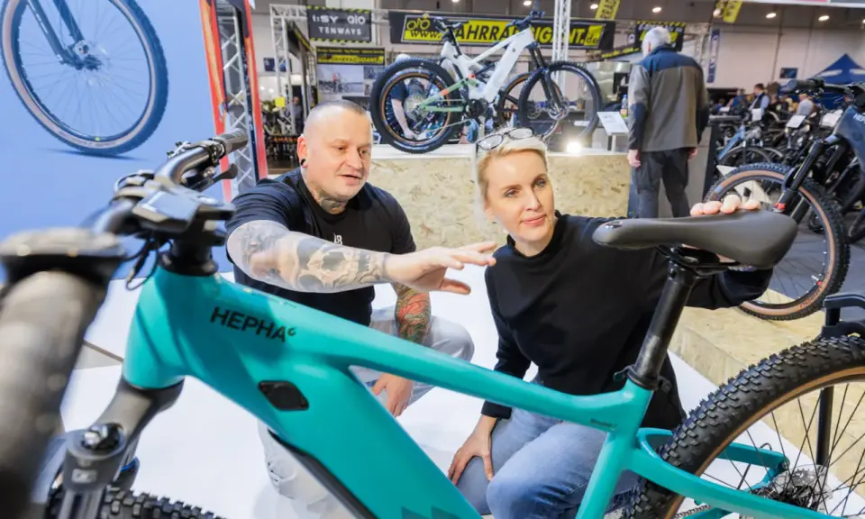 Ein Mann mit Tattoos und eine Frau begutachten auf der Fahrrad Messe ein türkisfarbenes E-Bike.