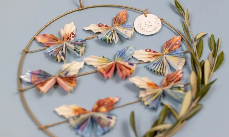 Kreative Deko: Viele bunte Schmetterlinge, gefaltet aus Geld, hängen an einem Ring. Ein schönes Geschenk, um Freude zu schenken.