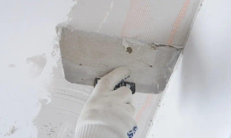 Ręka w rękawicy nakłada zaprawę na styropian przy suficie. Proces pokazujący, jak przykleić styropian do sufitu.