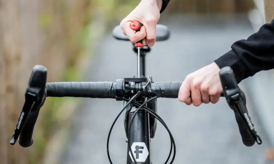 Hände stellen den MTB Lenker ein. Mit einem Schraubenzieher wird die Lenkerposition justiert, um die perfekte Fahrt zu ermöglichen.