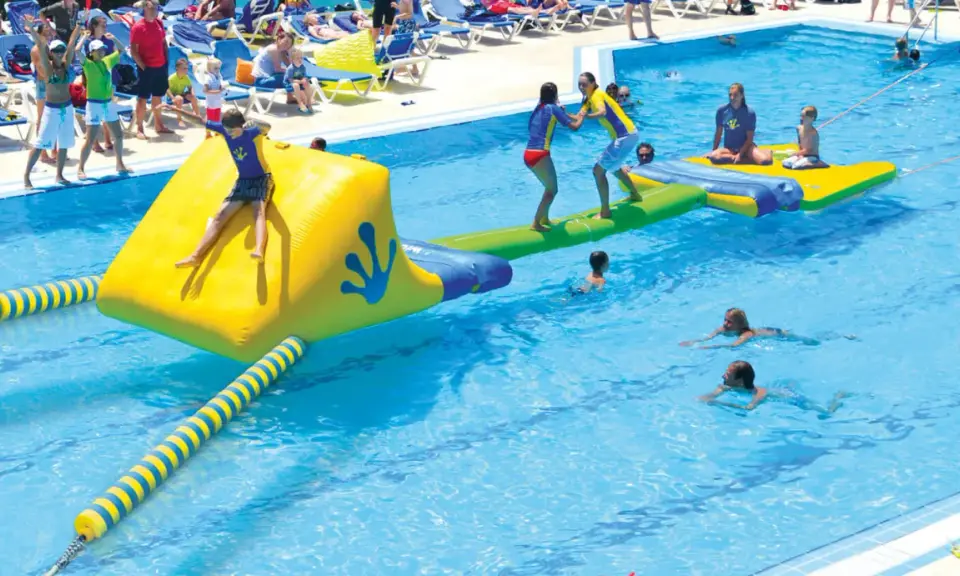 Kinder spielen auf einer aufblasbaren Wasserrutsche und im Pool eines Freibades.