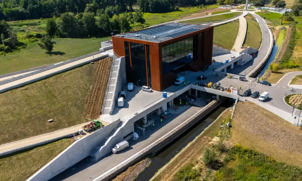 Nowoczesny budynek muzeum bitwy warszawskiej z cortenowską fasadą, otoczony zielenią i betonowymi konstrukcjami.