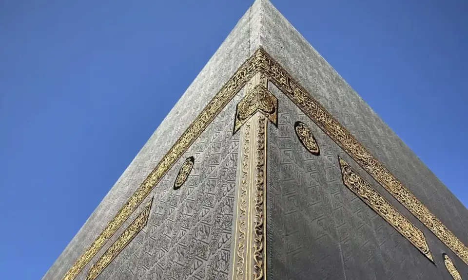 Die Kaaba in Mekka, Saudi-Arabien, mit ihrer schwarzen Hülle und goldenen Verzierungen vor blauem Himmel.