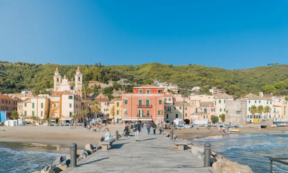 Laigueglia centro storico: case colorate affacciate sulla spiaggia, con una chiesa a due campanili e il mare azzurro.