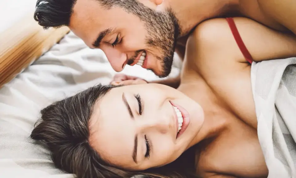 Pareja sonriente en la cama, disfrutando de intimidad.