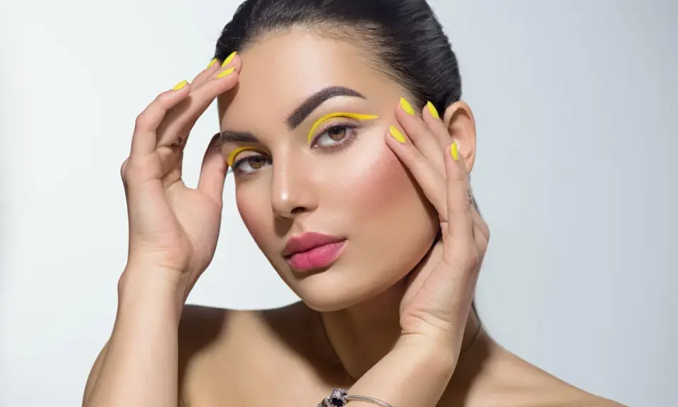 Mujer con un atrevido doble eyeliner amarillo y uñas a juego.
