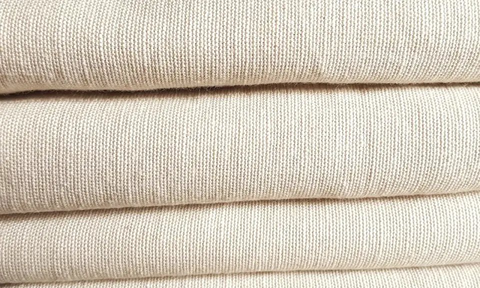 A stack of folded, natural-colored linen fabric. This image showcases the texture of linen, confirming that is linen a natural fiber.