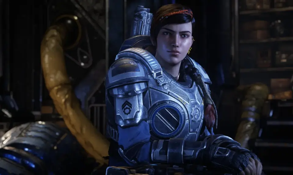 Kait Diaz w zbroi z Gears of War 5, z warkoczem i czerwoną opaską na włosach, w tle industrialne otoczenie.