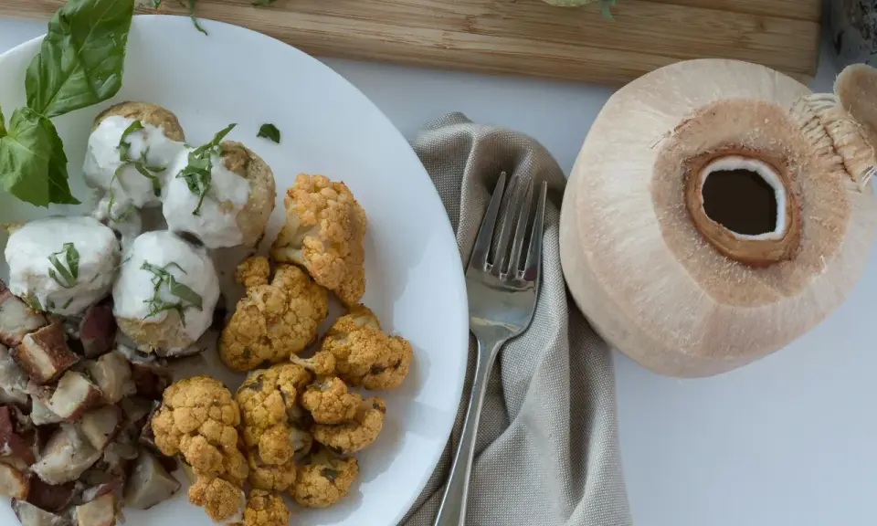 Talerz z klopsikami w sosie, pieczonym kalafiorem i ziemniakami, obok kokosa.
