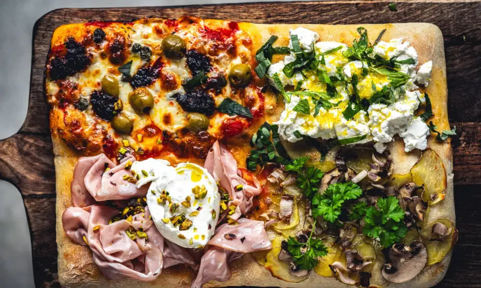 Vier verschiedene Beläge auf einer rechteckigen Pizza in Teglia: Oliven & Tomaten, Ricotta & Kräuter, Mortadella & Burrata, Kartoffeln & Pilze.