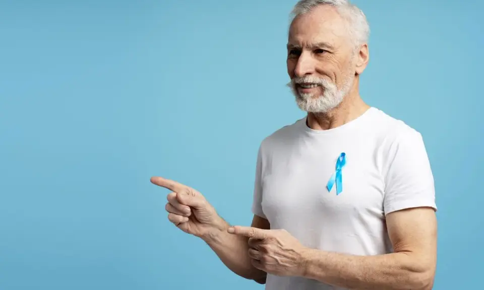 Starszy pan z niebieską wstążką na piersi, wskazujący palcami w lewo. To symbol walki z rakiem prostaty, ważnym tematem dla każdego psa 8.