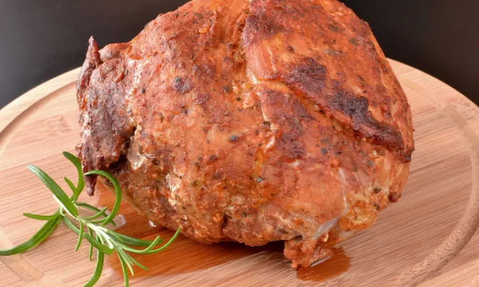 Pieczona szynka z ziołami, która wygląda jakby była przygotowana z użyciem marynaty do szynki. Gałązka rozmarynu dodaje aromatu.