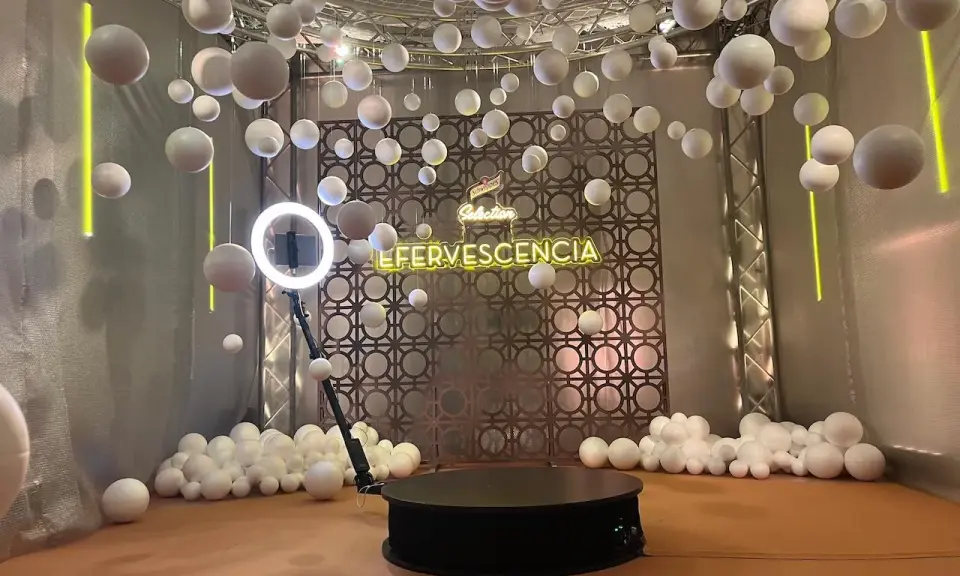Plataforma giratoria para fotos con luces de neón "EFERVESCENCIA" y esferas blancas colgantes, creando un efecto de bullet time.