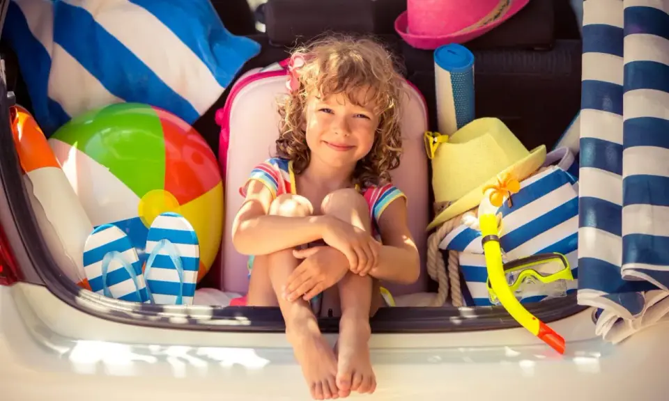 Niña sonriente rodeada de artículos de playa, lista para explorar nuevos sitios para ir con niños.