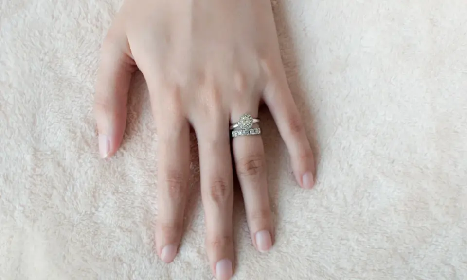 Mano femminile con due anelli scintillanti, uno con un grande diamante centrale e l'altro con pietre più piccole. Il dito anulare è il posto tradizionale dove si mette l'anello di fidanzamento donna.