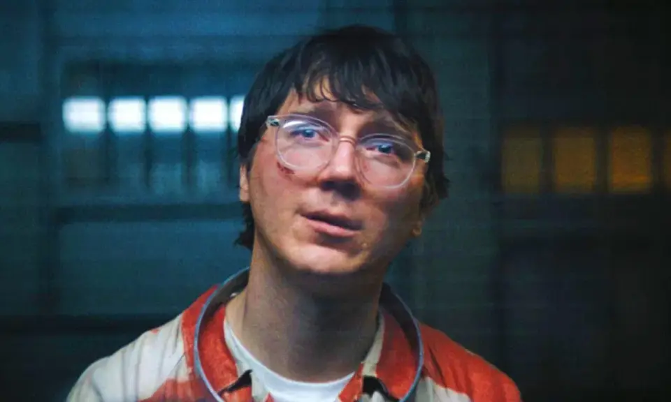 Paul Dano med glasögon och blodfläckar på sin randiga skjorta, i en mörk miljö med ljus bakom.