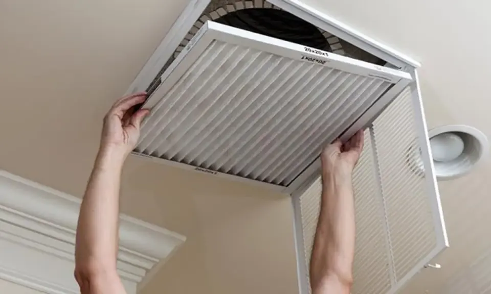 Man hands removing a pleated air filter from a ceiling vent. Essential for limpiar filtros aire acondicionado.