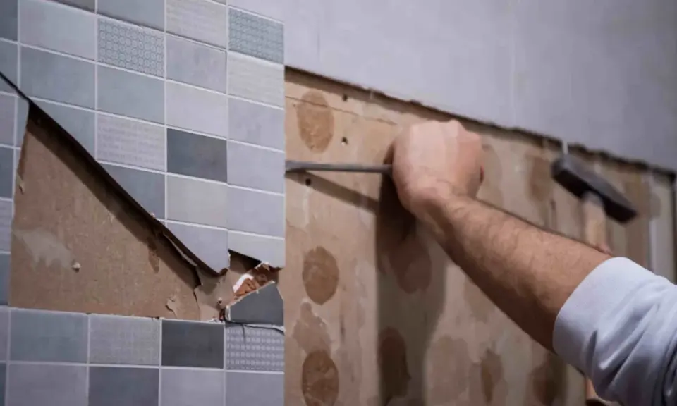 Persona usando una espátula para quitar azulejos de una pared.