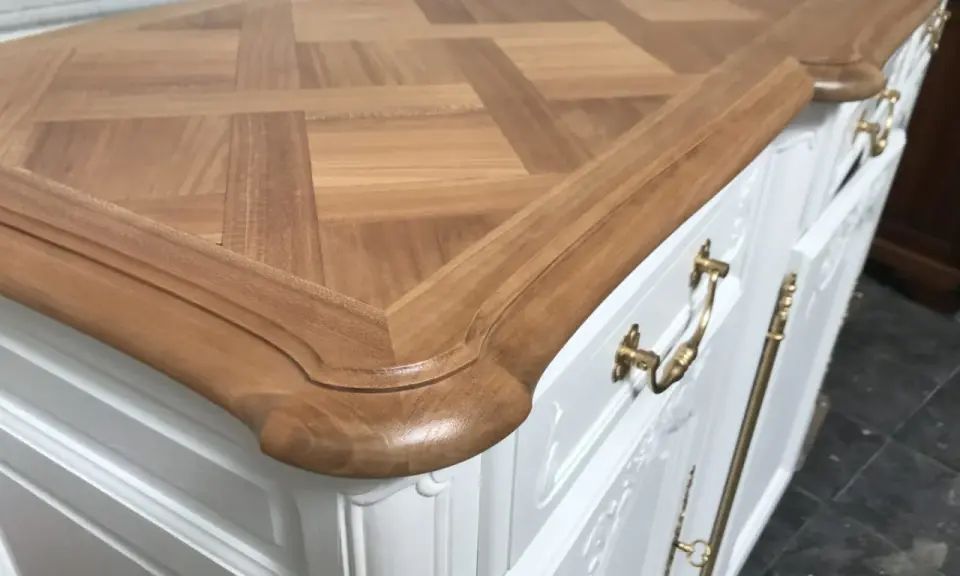 Un meuble ancien relooké en moderne, avec un plateau en bois clair à motif géométrique et des poignées dorées sur un corps blanc.