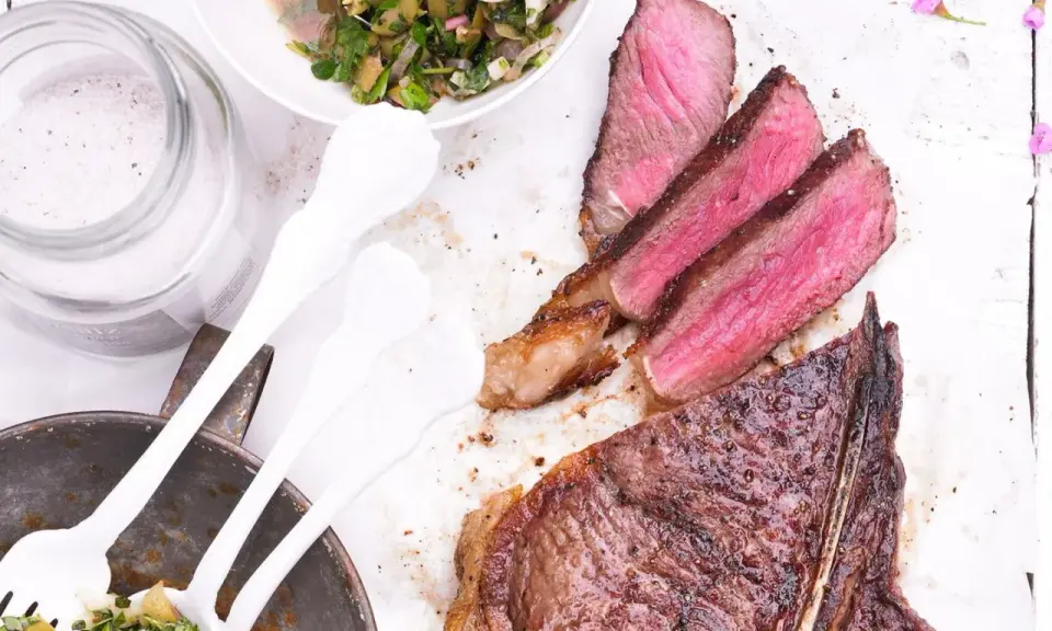 Perfekt gegrillter T-Bone-Steak, saftig rosa im Inneren, mit Beilagensalat und grobem Salz. Die t-bone steak zubereitung ist ein Genuss.