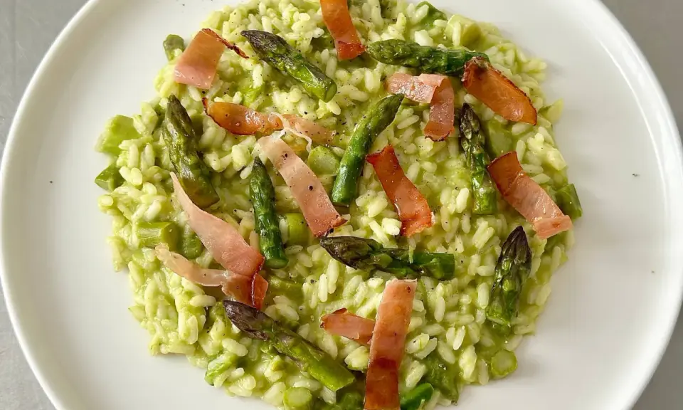 Risotto cremoso con asparagi freschi e croccanti strisce di speck, un piatto primaverile che delizia il palato.