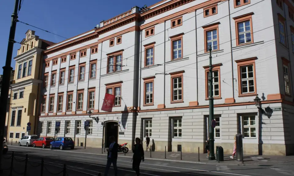 Uniwersytet Papieski w Krakowie, gdzie można studiować różne kierunki. Budynek z czerwonymi akcentami i flagą.