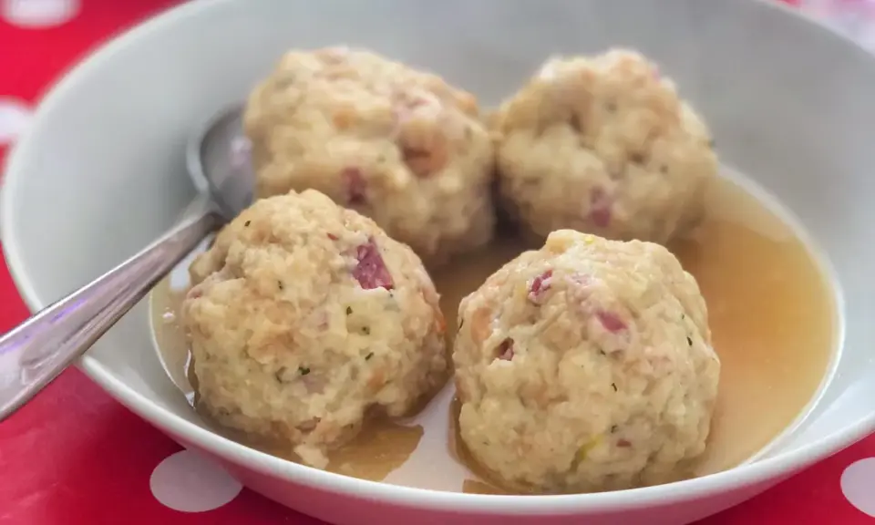 Canederli in brodo, uno dei piatti tipici del Trentino Alto Adige, serviti in una ciotola bianca su un tovagliolo rosso a pois bianchi.
