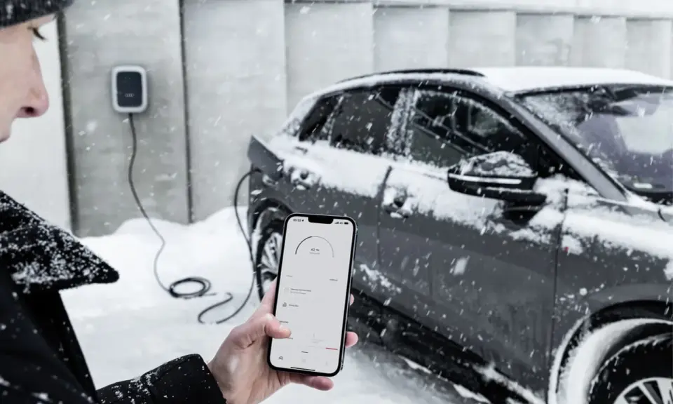 Persona controlla la carica di auto elettriche con lo smartphone, mentre nevica. Il freddo non ferma la tecnologia.