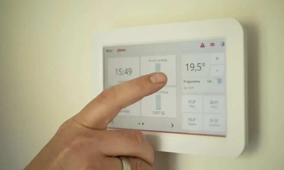 Un doigt interagit avec un écran tactile de domotique affichant la température et les programmes.