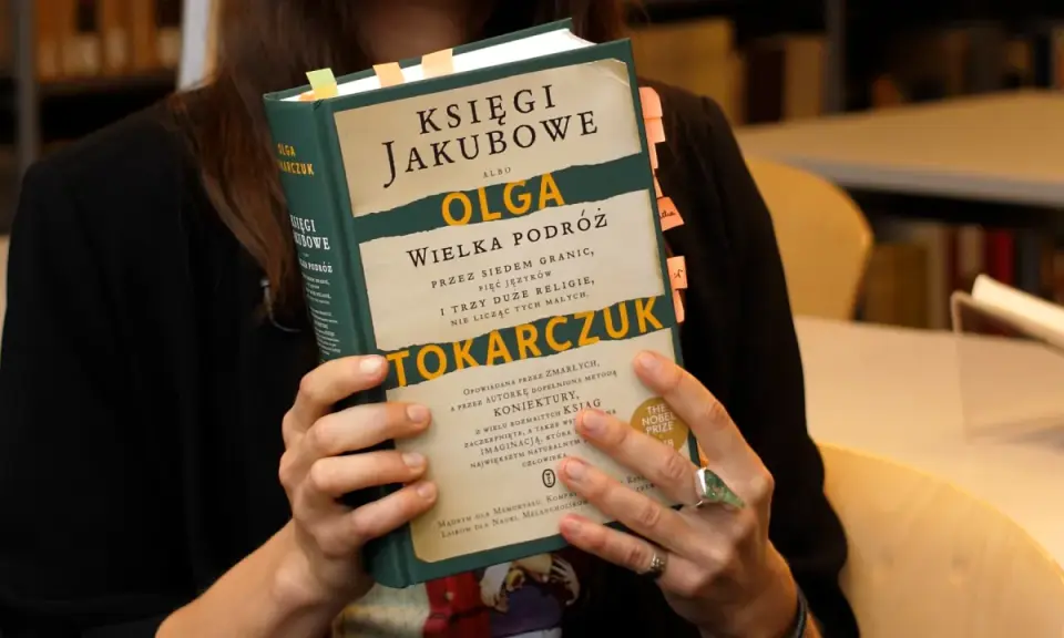 Osoba trzyma książkę "Księgi Jakubowe" Olgi Tokarczuk, z zakładkami w różnych kolorach.