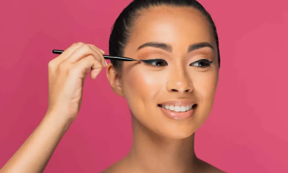 Une femme crée des "siren eyes" avec un eye-liner précis, son regard captivant promettant une beauté envoûtante.