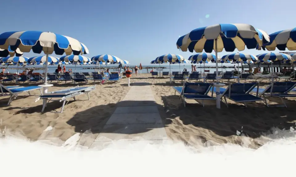 Ombrelloni a righe blu e bianche e lettini preparati per i visitatori al Delfini Beach Village Cattolica, con il mare sullo sfondo.