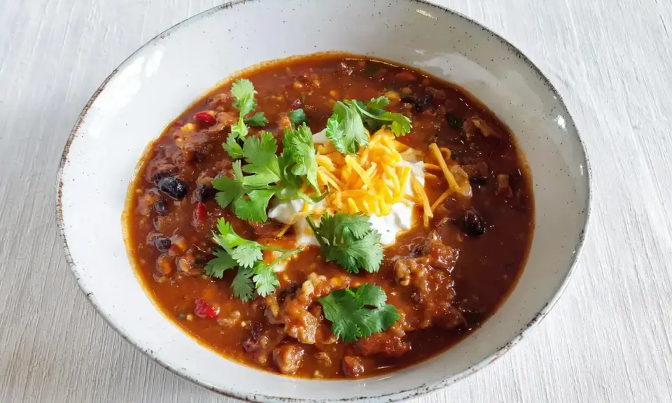 Gęste, aromatyczne chili con carne z fasolą, mięsem i przyprawami, udekorowane śmietaną, startym serem i świeżą kolendrą.