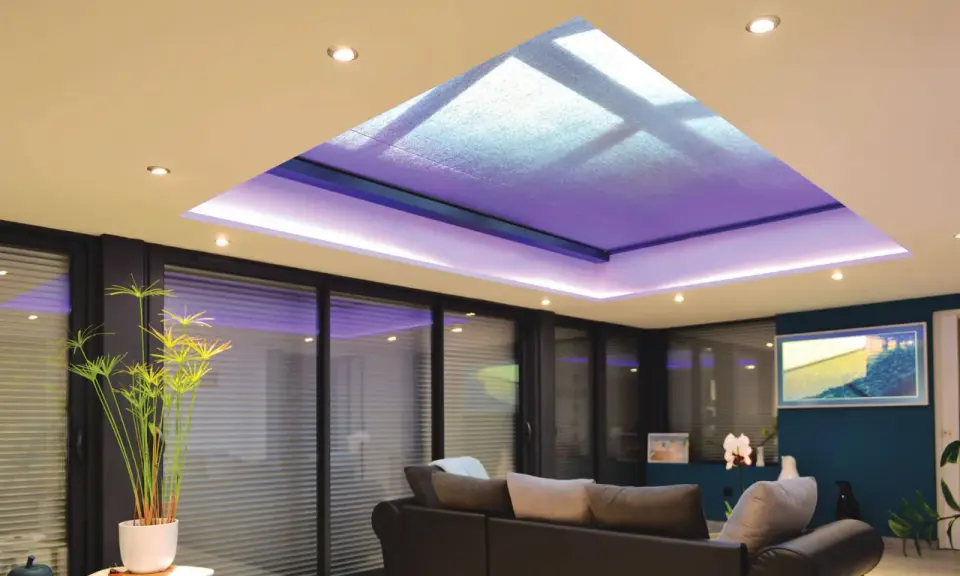 Salon moderne avec extension de maison et son puits de lumière illuminé de violet. Canapé confortable, plantes vertes et grandes baies vitrées.