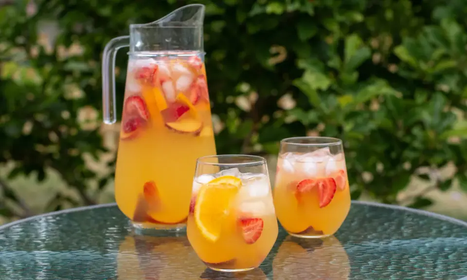 En karaff och två glas med en uppfriskande cava drink fylld med is, jordgubbar och apelsinskivor. Perfekt för en sommardag.