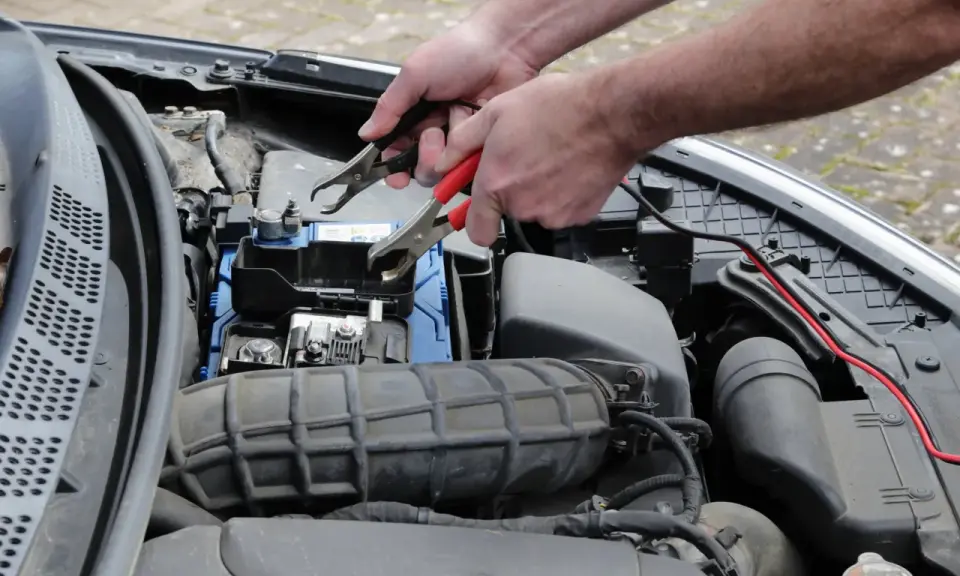 Ręce podłączają kable rozruchowe do akumulatora, próbując rozwiązać problem, dlaczego auto nie odpala.