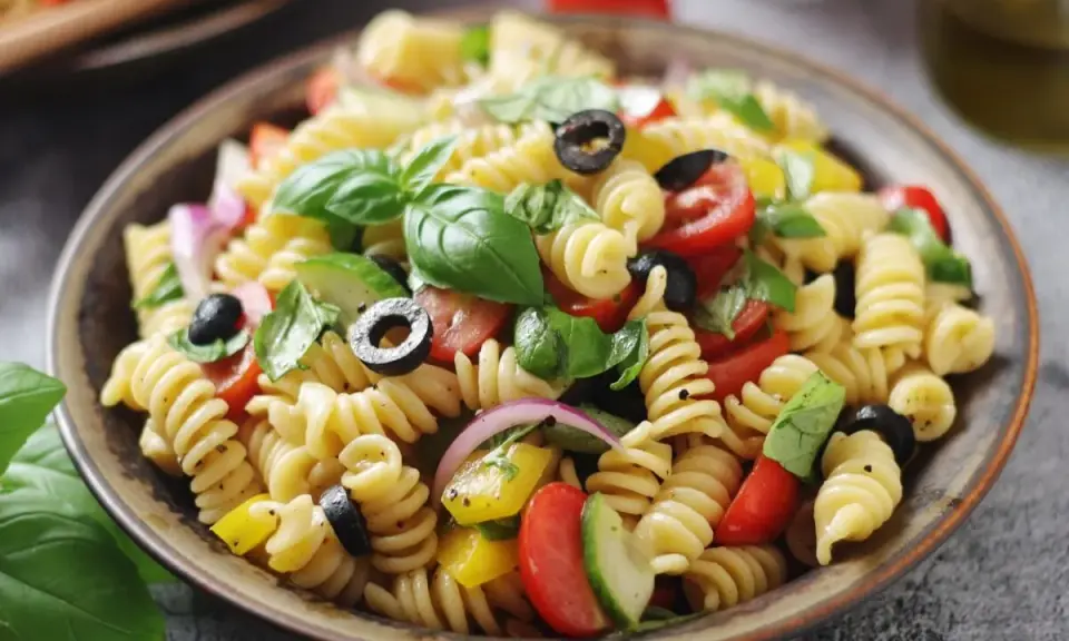 Un'insalata di pasta colorata con fusilli, pomodorini, olive nere, cipolla rossa, cetrioli e basilico fresco.