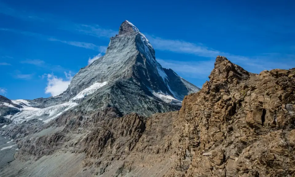 Majestatyczne szwajcaria góry z ośnieżonym szczytem Matterhorn w tle i skalistym zboczem na pierwszym planie.