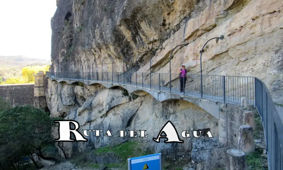 Un pontón de la oliva, parte de la Ruta del Agua, se aferra a un acantilado rocoso. Una mujer camina por el sendero con barandillas.