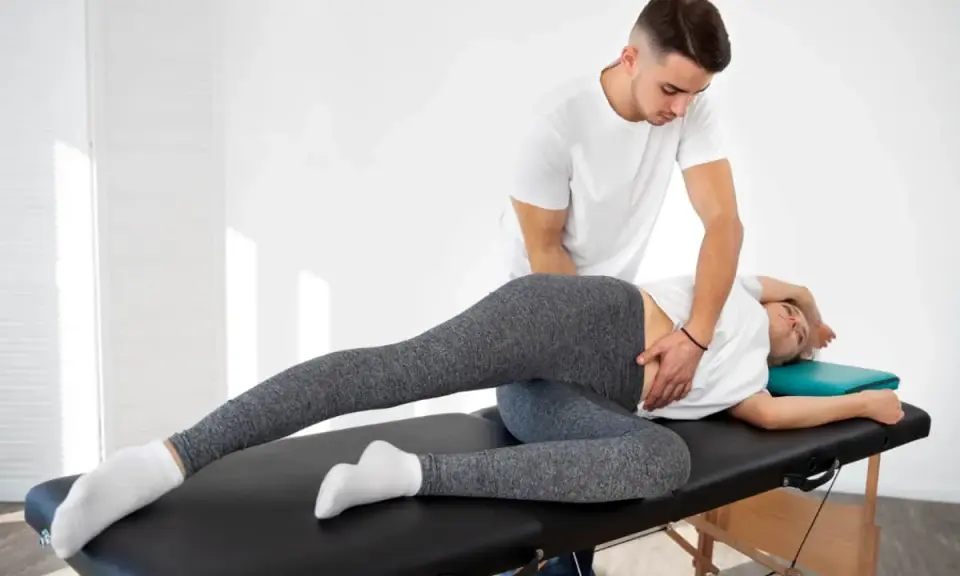 Fizjoterapeuta wykonuje terapię manualną, pomagając pacjentce w rozluźnieniu biodra. To właśnie terapia manualna co to jest – technika leczenia bólu i dysfunkcji.