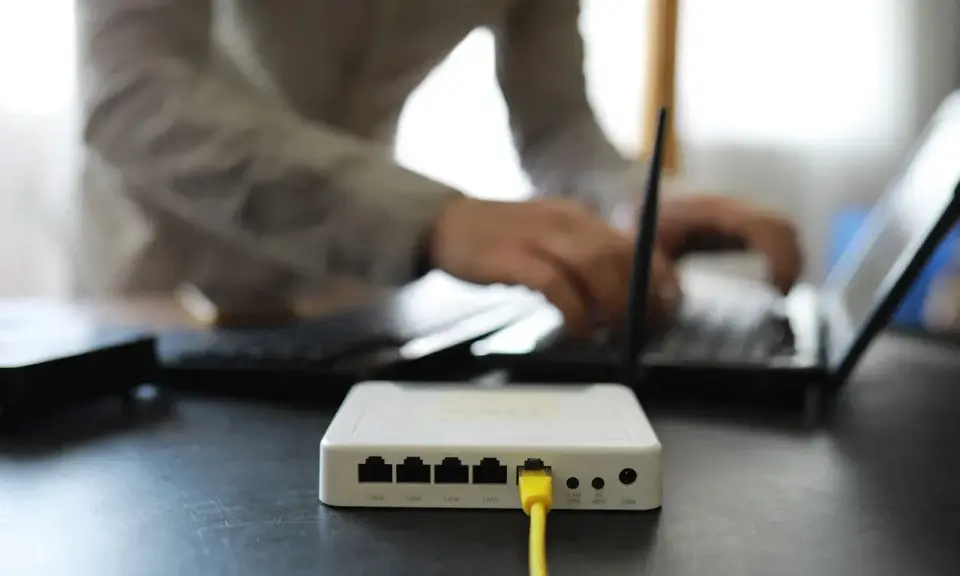 Connexion internet : faut il mettre les espaces pour la clé wifi ? Un routeur blanc est branché, une personne tape sur un ordinateur portable.