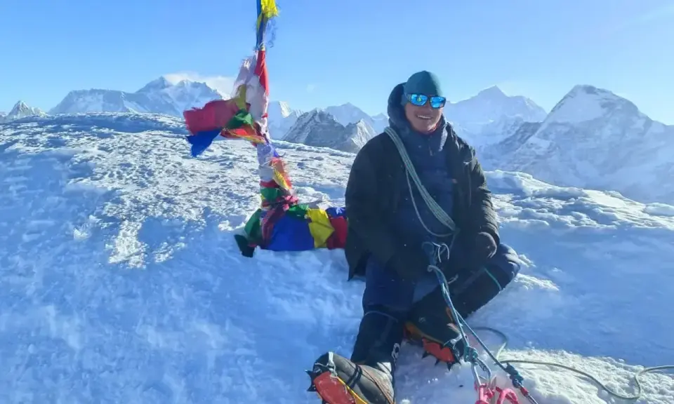 Szczęśliwy alpinista na szczycie Mera Peak, otoczony śniegiem i modlitewnymi flagami, z majestatycznymi górami w tle.