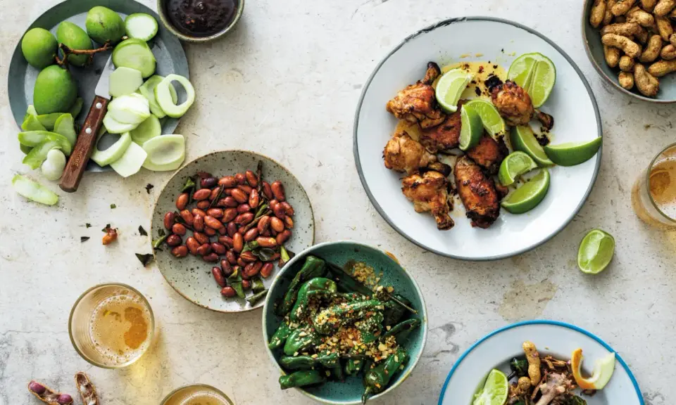 En härlig dukning med olika rätter av thai mat: kycklingvingar, friterade gröna paprikor, jordnötter och omogna mangos.