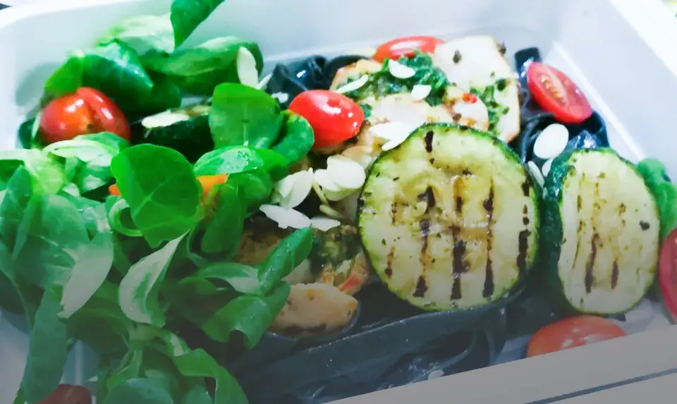 Kolorowy catering dietetyczny z grillowaną cukinią, pomidorkami i zielonymi liśćmi. Dowiedz się, jak podgrzewać catering dietetyczny, by zachować świeżość.